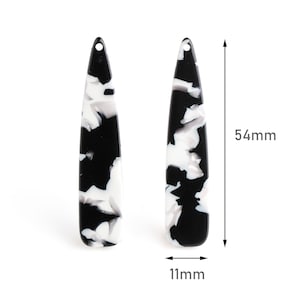 Może przedstawiać: Para czarno-białych marmurowych kolczyków akrylowych. Każdy kolczyk ma 5,4 cm długości i 1,1 cm szerokości.