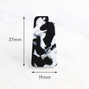 Puede incluir: Pendiente rectangular de mármol negro y blanco con un agujero en la parte superior. El pendiente mide 37 mm de alto y 19 mm de ancho.