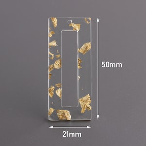 May include: A clear rectangular acrylic charm with gold leaf flakes embedded inside. The charm has a rectangular opening in the center. The charm measures 2.0 inches by 1.9 inches.
