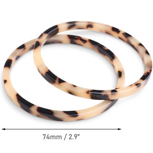 May include: Two tortoiseshell patterned plastic bangles. The bangles are stacked on top of each other. The bangles are 2.9 inches in diameter.