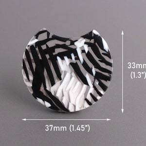 May include: Black and white abstract patterned acrylic resin half-circle pendant measuring 1.45 inches wide and 1.3 inches tall.