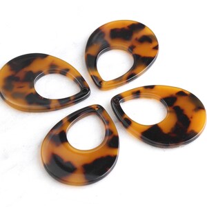 May include: Four brown and black tortoise shell teardrop shaped resin pendants with a hole at the top.