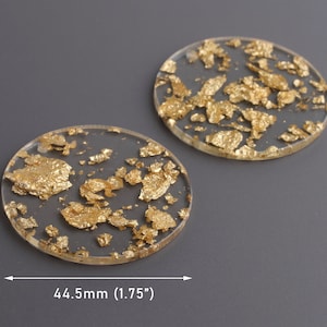 Puede incluir: Dos posavasos redondos de resina transparente con escamas de pan de oro incrustadas. Los posavasos tienen un diámetro de 4,45 cm.