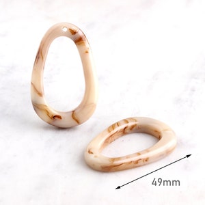 May include: Two oval-shaped, marbled resin pendants in cream and brown tones. One pendant is upright, the other is lying down. The pendants are approximately 1.9 inches long. Each has a small hole at the top for stringing.