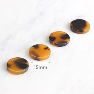 May include: Four brown and black round resin pendants with a hole at the top. The pendants are 15 mm in diameter.