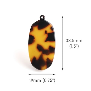 Puede incluir: Un colgante ovalado de carey marrón y amarillo con un agujero en la parte superior. El colgante mide 38,5 mm de alto y 19 mm de ancho.