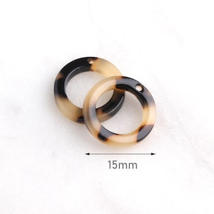 Könnte beinhalten: Zwei runde Schmuckkomponenten aus Acryl mit Schildpattmuster. Jeder Ring hat ein kleines Loch zum Auffädeln. Der Durchmesser beträgt 15 mm.