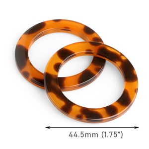 May include: Two round, tortoise shell-patterned acrylic rings, each 1.75 inches in diameter, are displayed against a white background. The rings are a warm brown color with dark brown spots. The rings are designed for crafting or jewelry making.