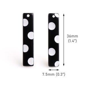 May include: Two black and white polka dot rectangular acrylic charms with a hole at the top. Each charm measures 1.4 inches in length and 0.3 inches in width.