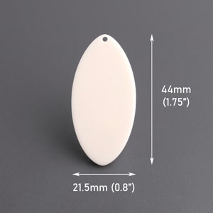 May include: A cream-coloured, oval-shaped pendant with a small hole for stringing. The pendant measures 44mm in length and 21.5mm in width. The smooth surface reflects light, suggesting a polished finish.