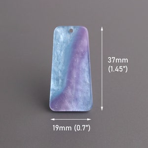 Könnte beinhalten: Ein hellblauer und lilafarbener Harzanhänger mit einem weißen Wirbel und Glitzer. Der Anhänger ist 37 mm hoch und 19 mm breit.