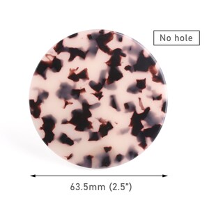 May include: A round, 2.5 inch, white and black tortoiseshell hair clip with no hole. "No hole" is written in black text on a white rectangle.