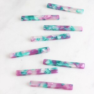 May include: A set of eight colorful, rectangular, marbled acrylic beads. The beads are a mix of white, pink, and green.