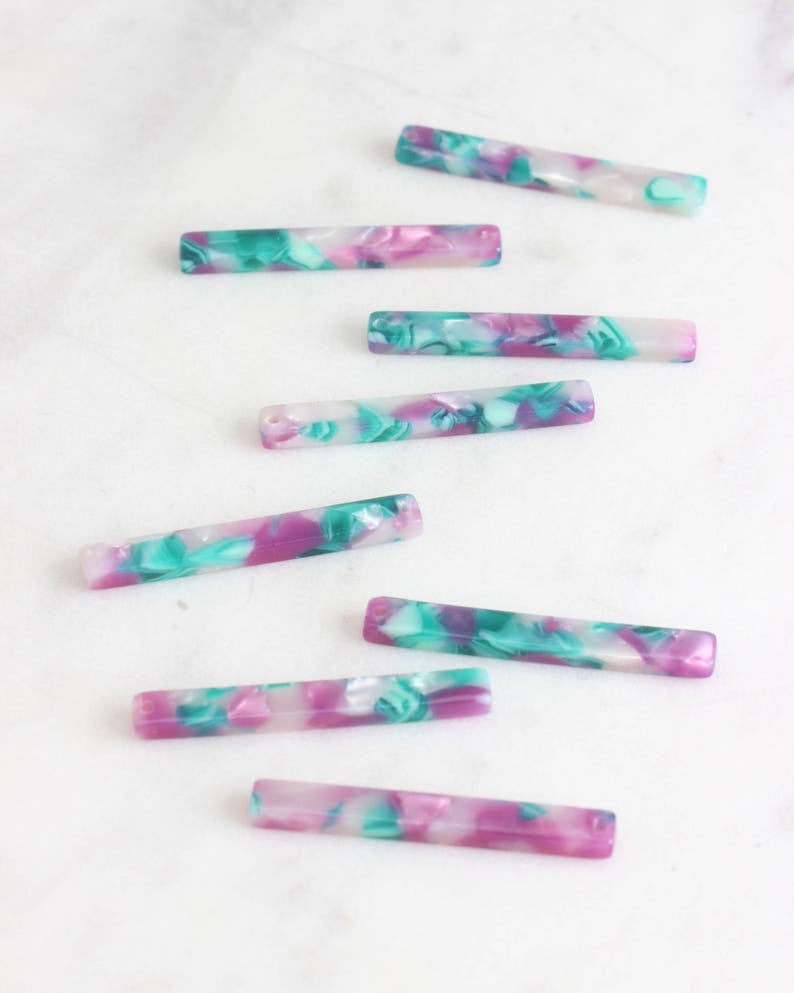 May include: A set of eight colorful, rectangular, marbled acrylic beads. The beads are a mix of white, pink, and green.