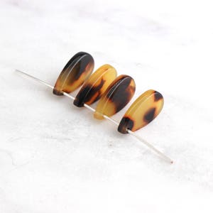May include: Four brown and yellow teardrop-shaped beads with a mottled pattern, strung on a silver wire.