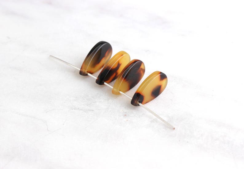 May include: Four brown and yellow teardrop-shaped beads with a mottled pattern, strung on a silver wire.