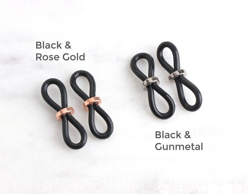 May include: Two pairs of black rubber glasses strap holders with metal accents. One pair has rose gold accents and the other has gunmetal accents. Black & Rose Gold and Black & Gunmetal text is visible.