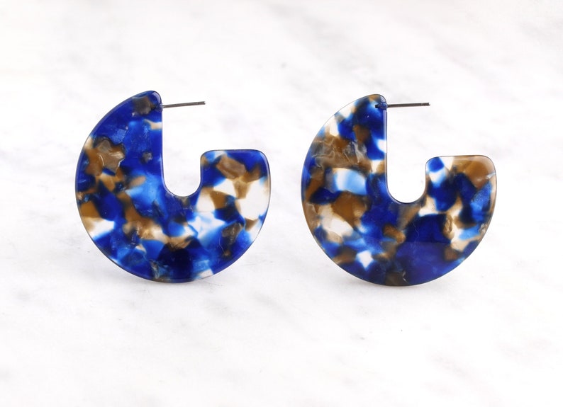 Op de afbeelding: Een paar blauwe, witte en bruine gepatroneerde creolen. De oorbellen zijn gemaakt van een lichtgewicht materiaal en hebben een uniek, abstract ontwerp.