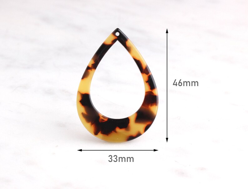 May include: A brown and yellow teardrop-shaped pendant with a hole at the top. The pendant is 46 mm tall and 33 mm wide.