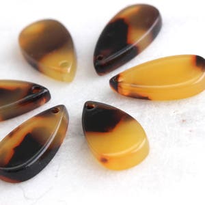 May include: Six brown and yellow teardrop-shaped resin pendants with a mottled pattern.