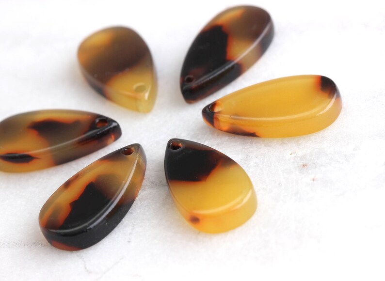 May include: Six brown and yellow teardrop-shaped resin pendants with a mottled pattern.