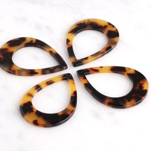 May include: Four brown and black teardrop-shaped resin pendants with a hole in the center. The pendants have a mottled pattern.