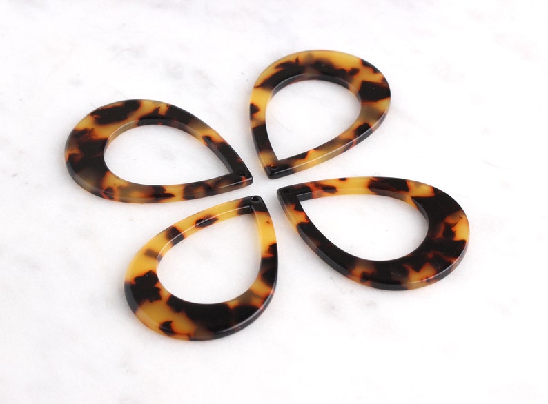 May include: Four brown and black teardrop-shaped resin pendants with a hole in the center. The pendants have a mottled pattern.