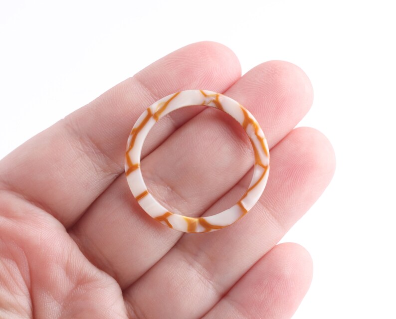 May include: A white ring with brown marbling. The ring is made of shell and has a smooth, polished finish.