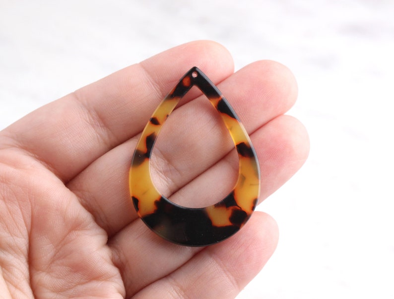 May include: A brown and black tortoise shell teardrop shaped pendant with a hole at the top for hanging.