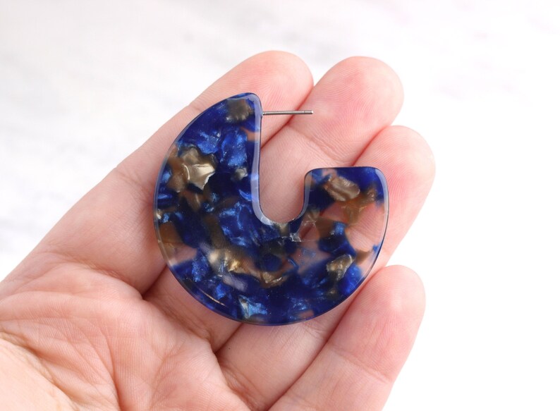 Op de afbeelding: Blauwe en gouden resin creolen met een uniek, abstract patroon.