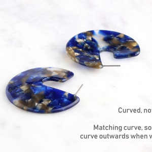 Op de afbeelding: Een paar blauwe, witte en gouden marmeren creolen. De creolen zijn gebogen, niet plat, en hebben een overeenkomende bocht, zodat ze beide naar buiten buigen wanneer ze worden gedragen.