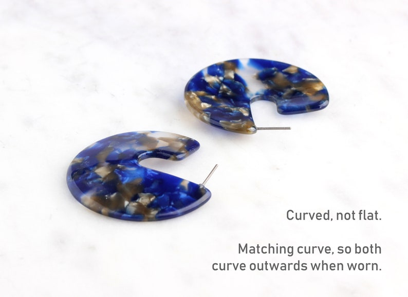 Op de afbeelding: Een paar blauwe, witte en gouden marmeren creolen. De creolen zijn gebogen, niet plat, en hebben een overeenkomende bocht, zodat ze beide naar buiten buigen wanneer ze worden gedragen.