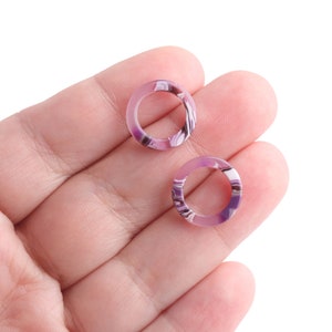 K&ouml;nnte beinhalten: Zwei purpurfarbene und wei&szlig;e marmorierte Ringe, die in einer Hand gehalten werden.