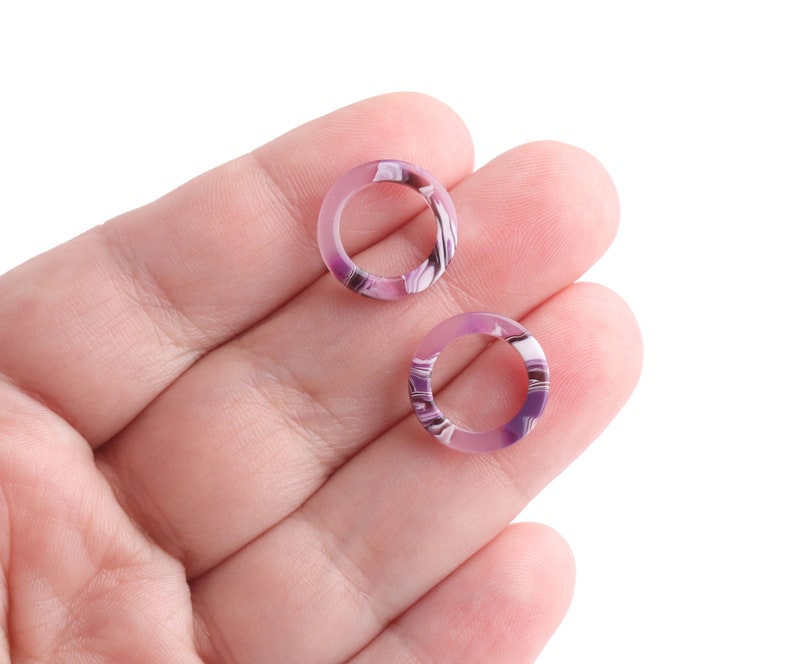 K&ouml;nnte beinhalten: Zwei purpurfarbene und wei&szlig;e marmorierte Ringe, die in einer Hand gehalten werden.