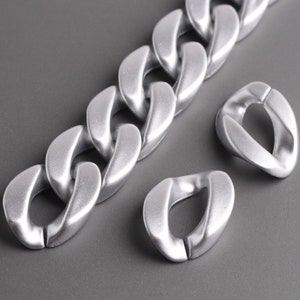Pu&ograve; includere: Una collana a catena argentata con grandi maglie spesse. La catena &egrave; realizzata in metallo liscio e lucido e presenta un design moderno e minimalista.
