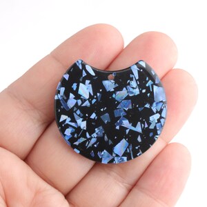 May include: A black resin pendant with a half-circle shape and a hole at the top for hanging. The pendant is covered in blue iridescent glitter.