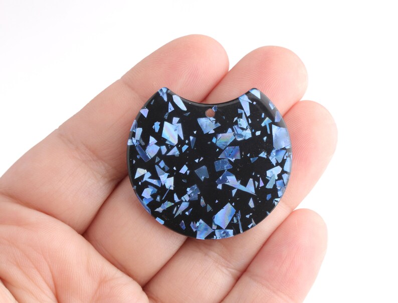 May include: A black resin pendant with a half-circle shape and a hole at the top for hanging. The pendant is covered in blue iridescent glitter.