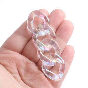May include: A clear iridescent plastic chain with multiple links. The chain is held in a hand.
