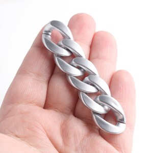 Pu&ograve; includere: Un anello di catena argentato con una finitura liscia e piatta. La catena &egrave; in metallo e ha un design spesso e audace.
