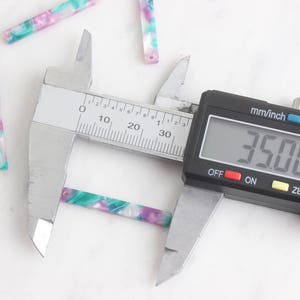 May include: A close-up of a digital caliper measuring a small, colorful, rectangular piece of material. The caliper reads 3.500 mm.