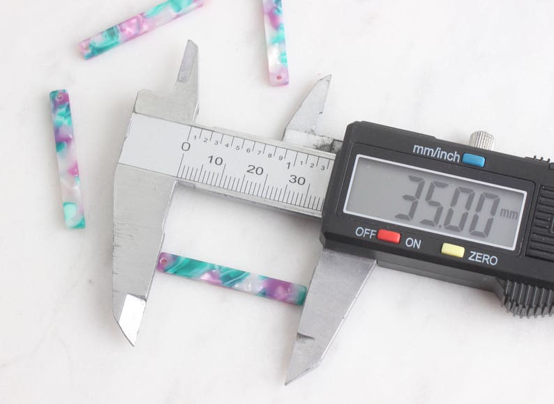May include: A close-up of a digital caliper measuring a small, colorful, rectangular piece of material. The caliper reads 3.500 mm.