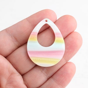 May include: A pastel-colored teardrop-shaped pendant with a hole at the top. The pendant has stripes of pink, yellow, and blue.