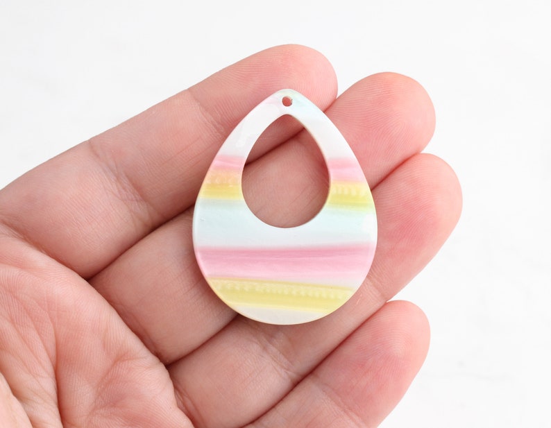 May include: A pastel-colored teardrop-shaped pendant with a hole at the top. The pendant has stripes of pink, yellow, and blue.