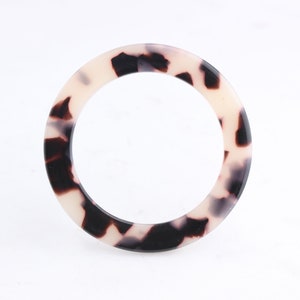 May include: A white and black tortoiseshell patterned plastic bangle bracelet.