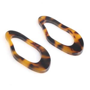 May include: Two open teardrop-shaped acrylic earring components. The earrings have a tortoiseshell pattern with shades of brown and black. Each component has a small hole at the top for attachment.