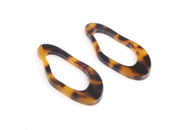 May include: Two open teardrop-shaped acrylic earring components. The earrings have a tortoiseshell pattern with shades of brown and black. Each component has a small hole at the top for attachment.
