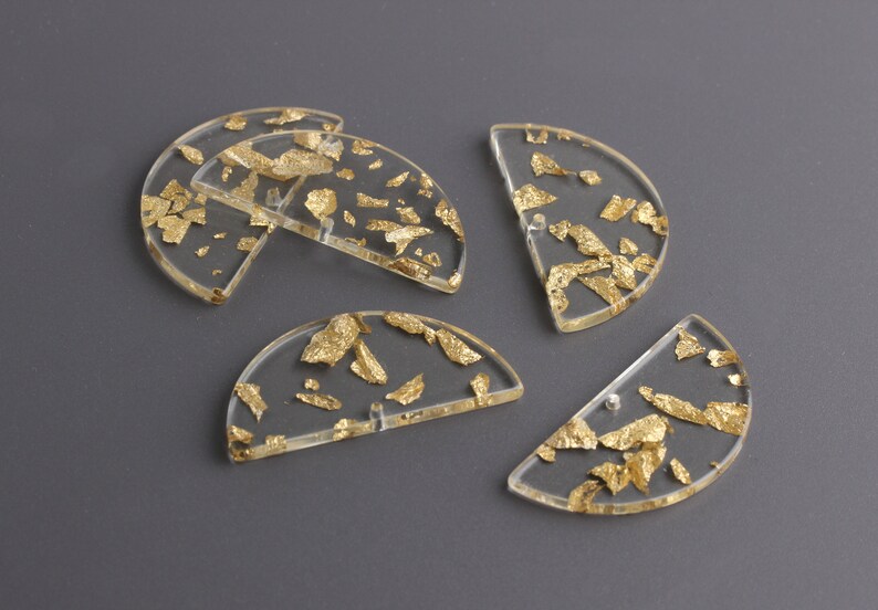 Puede incluir: Cinco formas de medio c&iacute;rculo de acr&iacute;lico transparente con escamas de pan de oro incrustadas. Las formas tienen un di&aacute;metro de aproximadamente 5 cm.