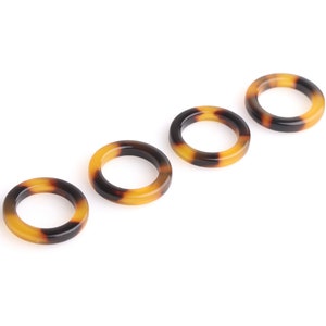 May include: Four brown and black tortoiseshell hair rings. The rings are arranged in a row, with the largest ring on the left and the smallest ring on the right.