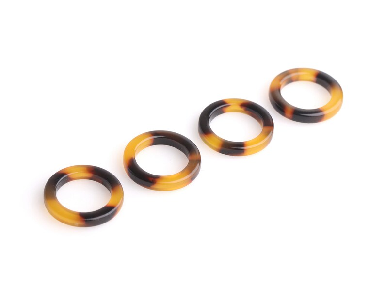 May include: Four brown and black tortoiseshell hair rings. The rings are arranged in a row, with the largest ring on the left and the smallest ring on the right.