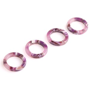 K&ouml;nnte beinhalten: Vier purpurfarbene und wei&szlig;e marmorierte Kunststoffringe. Die Ringe sind in einer Reihe angeordnet, wobei der gr&ouml;&szlig;te Ring links und der kleinste Ring rechts ist.